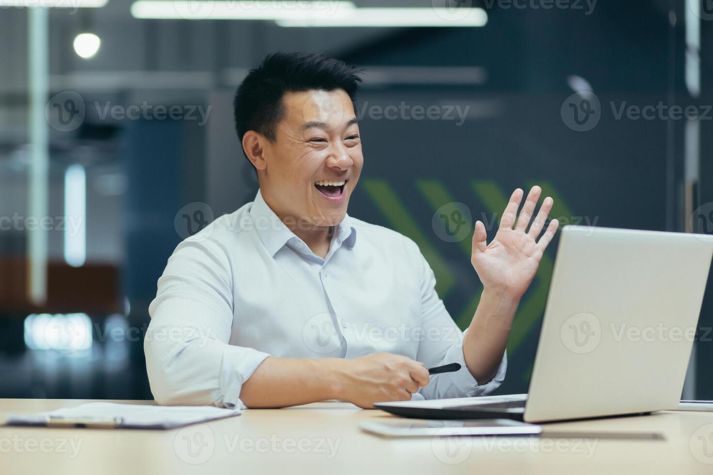 Happy and successful asian boss talking with colleagues on call, using laptop, waving hands greeting to camera, businessman at work. photo
