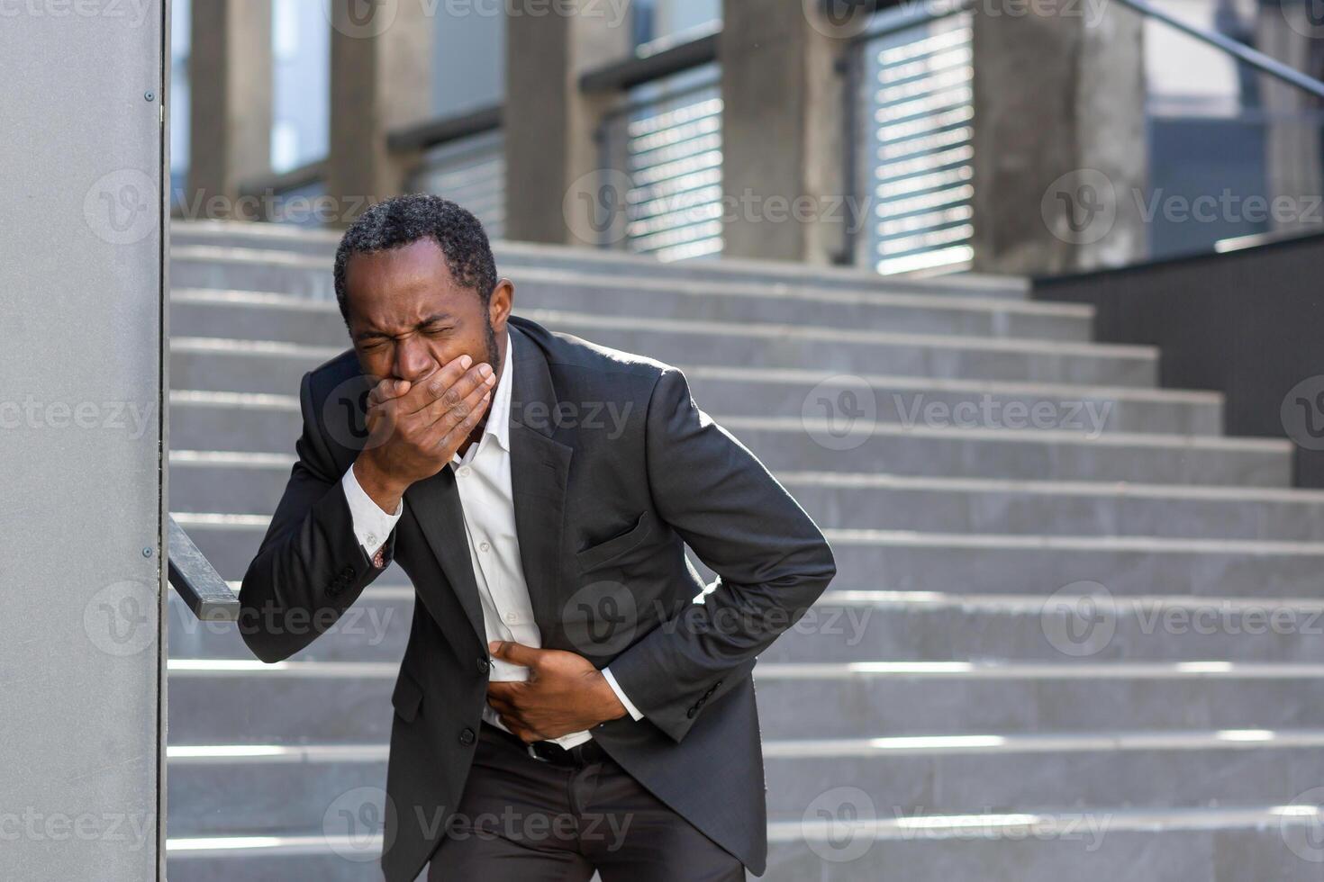 Nausea and pain in the stomach, a businessman from outside the office building is sick, a man is holding his hand on his stomach in a business suit, he got sick with poor-quality food. photo