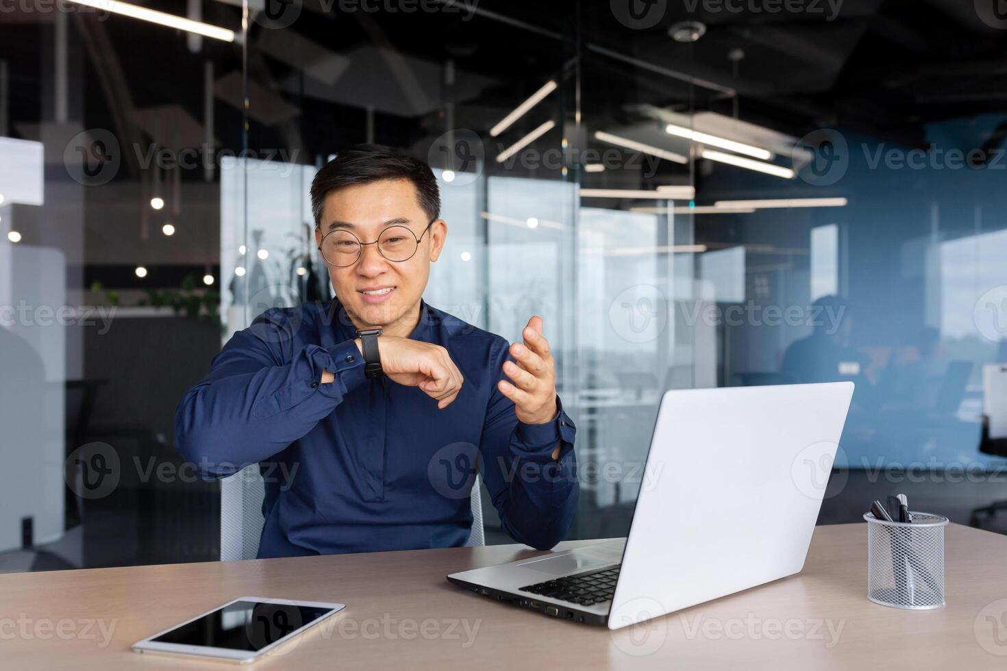Cheerful and smiling online customer support tech worker, Asian man with call headset smiling and looking at webcam, working on helpline and consulting customers, using headset. photo