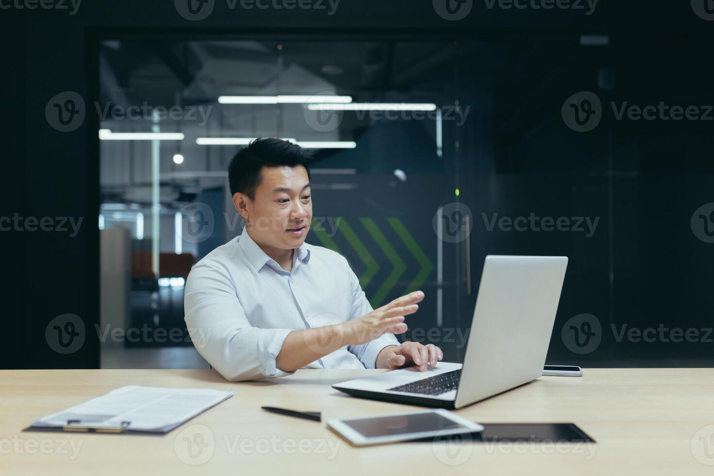 A serious young man, an Asian businessman, a freelancer, talks via call from a laptop with clients and partners. Sitting at a desk in a modern office photo