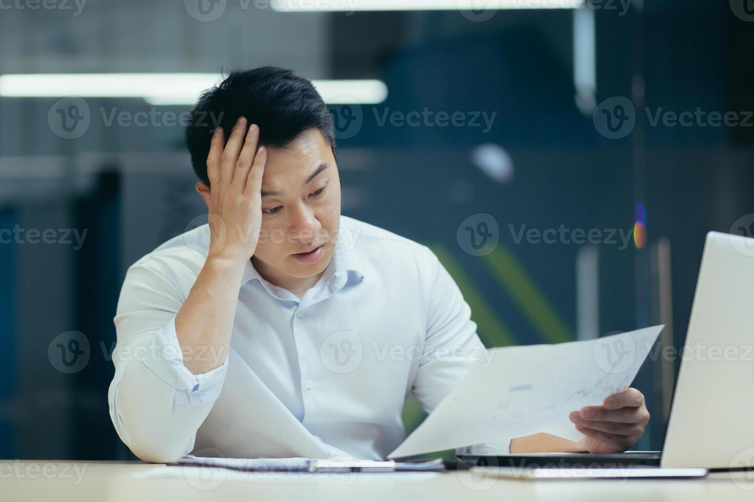 Stressed businessman holding face with his hands because having trouble. Bankrupt Asian Male is sitting with laptop computer and paperwork on desk at workplace in office. Business Mistake Financial photo