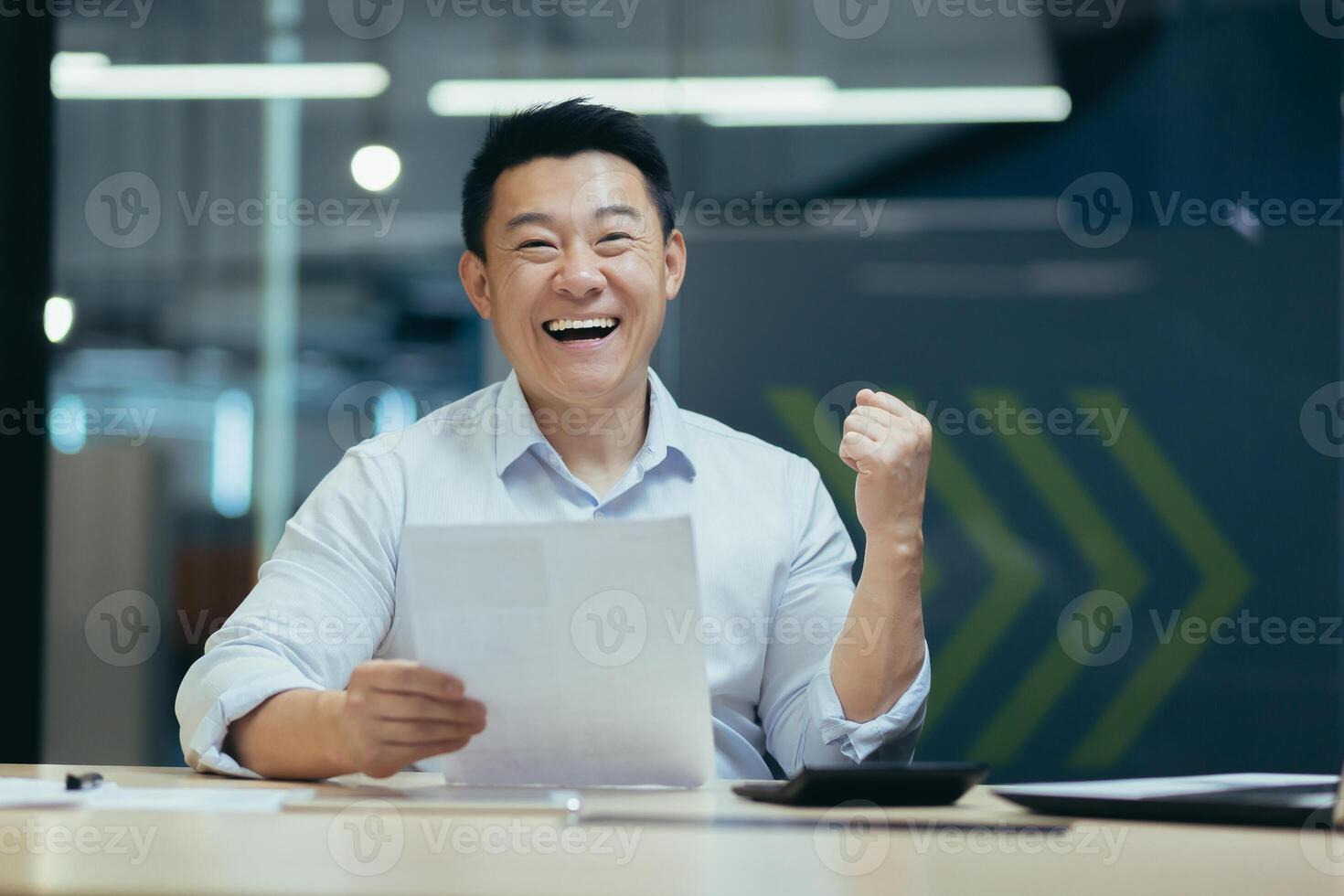 Portrait of successful asian businessman boss, man smiling and looking at camera, holding letter and document in hands, happy with success holding hand up gesture of triumph and victory photo