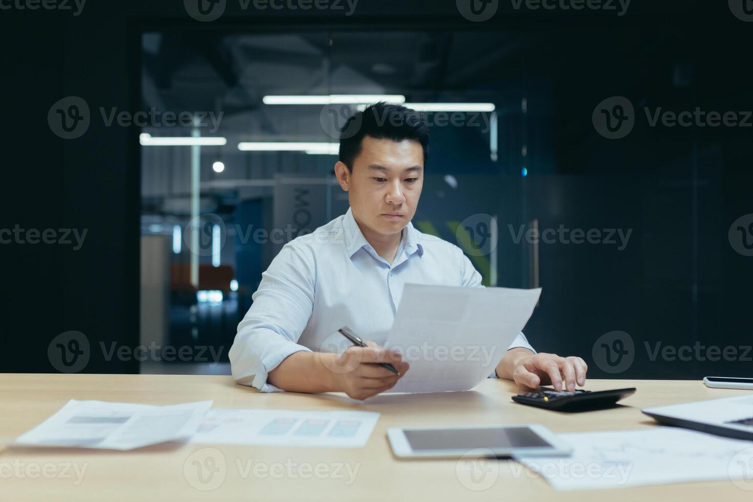 Young Asian male accountant working with documents and calculator. Sitting at a desk with a laptop in a modern office photo
