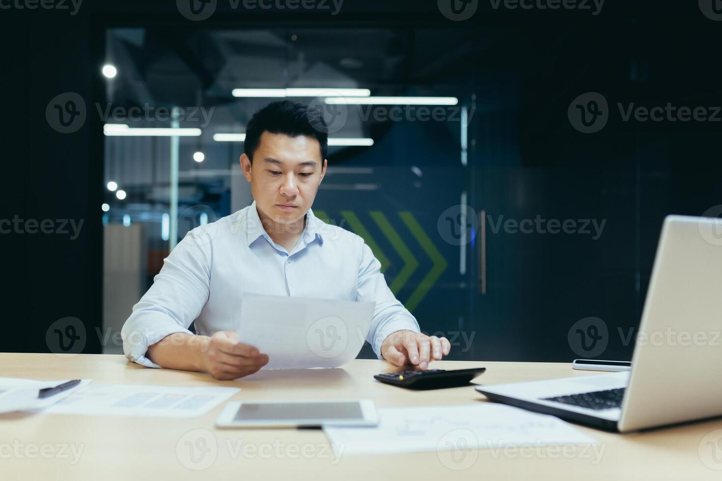 Young Asian male accountant working with documents and calculator. Sitting at a desk with a laptop in a modern office photo