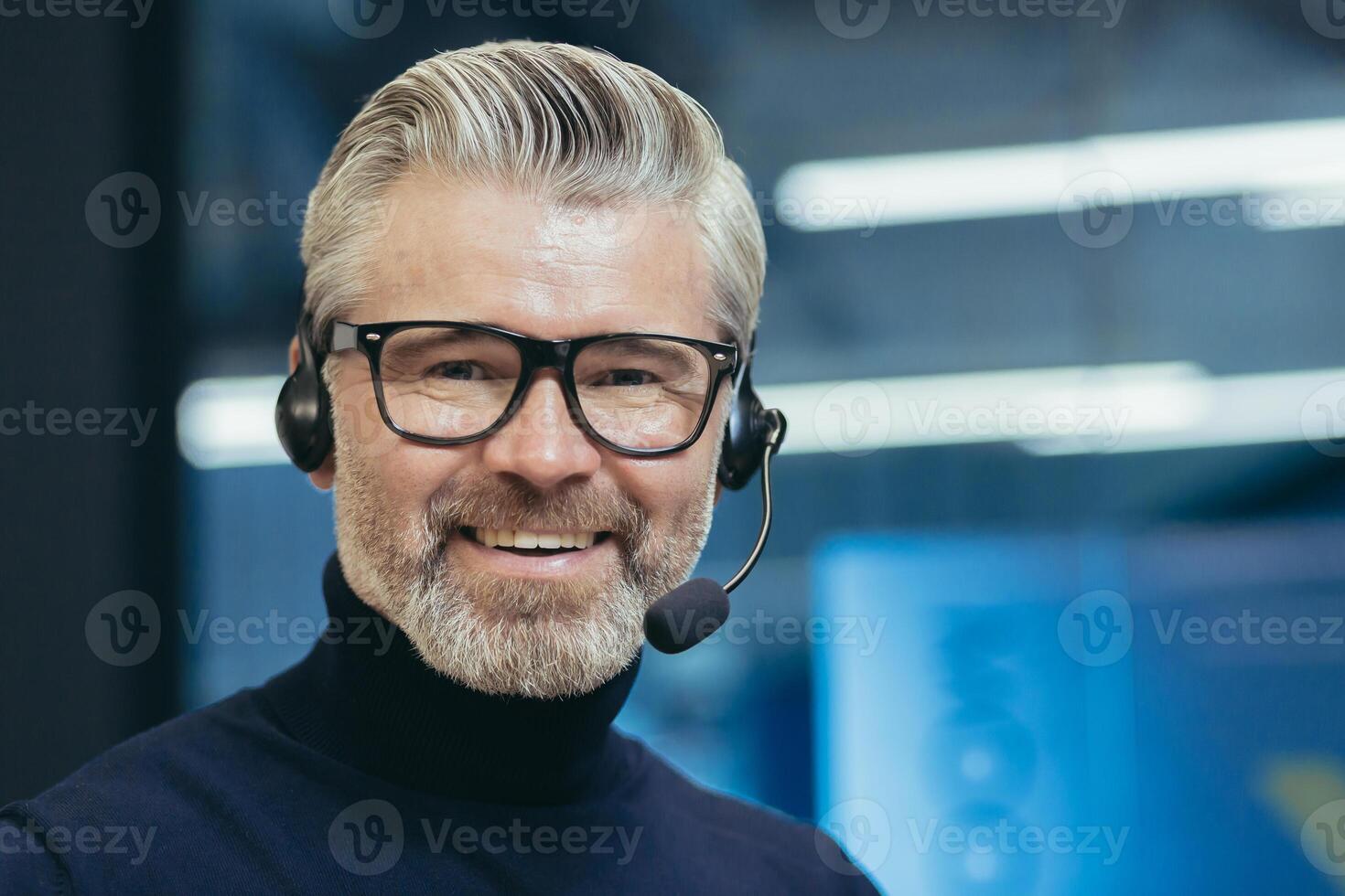 Closeup portrait of senior mature boss with headset, call, man smiling and looking at camera, gray haired businessman wearing glasses manager investor working inside modern office building, photo