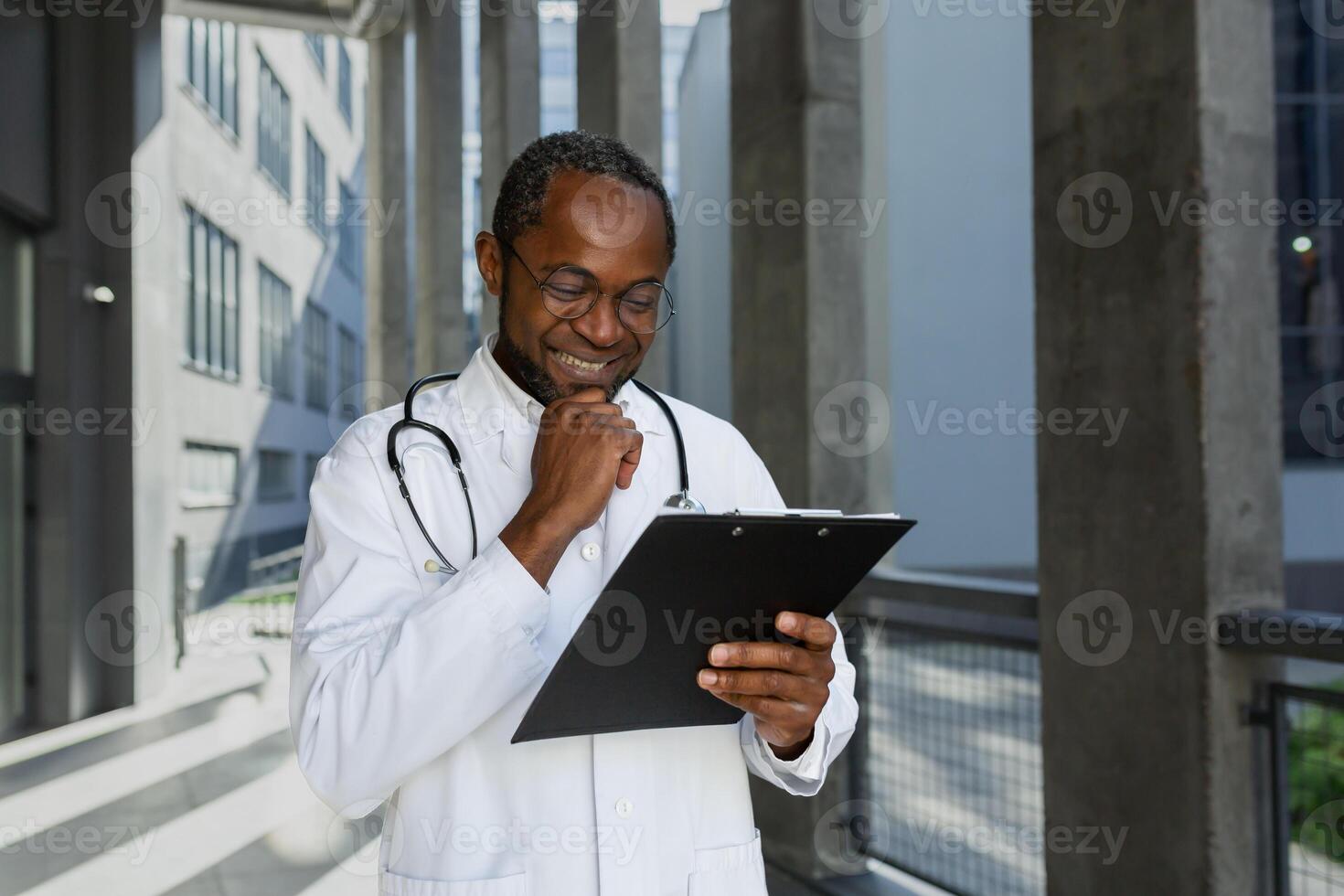 Happy and smiling mature doctor reading report documents outside clinic, african american man in medical coat and stethoscope and glasses, satisfied with patient's treatment result. photo