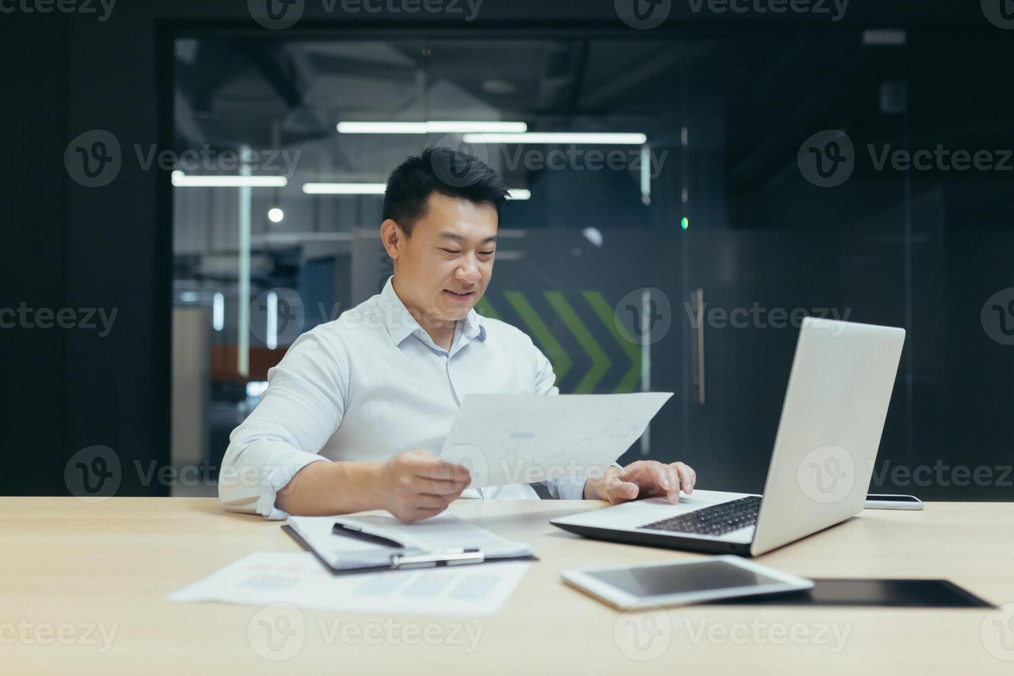 Office work. A young Asian man is working on a laptop and documents while sitting at a table. photo