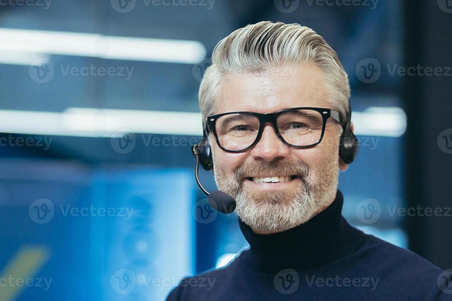 Portrait of a gray-haired handsome man in glasses and a headset with a microphone. Speaker, business trainer, online conference. Looking at the camera, smiling. photo