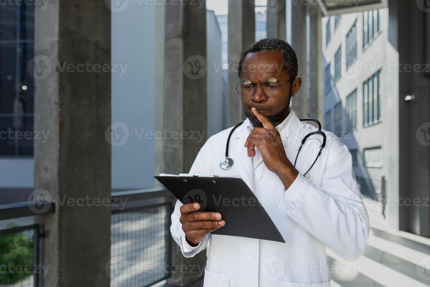 Serious and thinking mature african american doctor outside modern clinic, thinking and reading treatment report and documents. photo