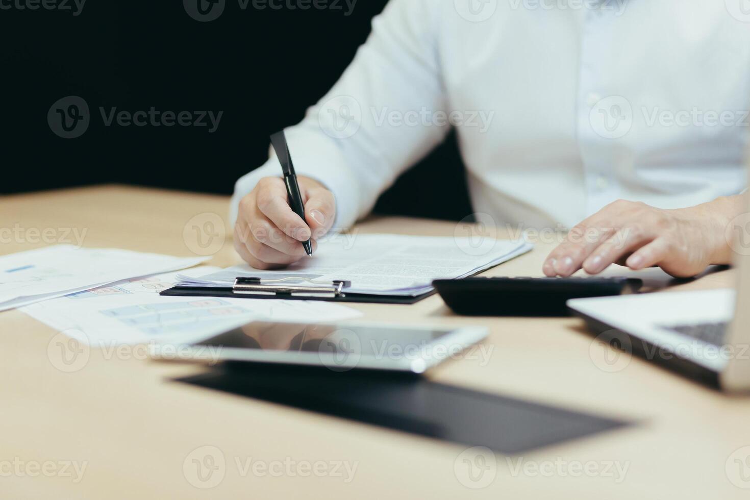 Close-up photo. Man's hands in a white shirt of an accountant, auditor, financier, banker working in the office at a table with documents and with a laptop, using a calculator. photo