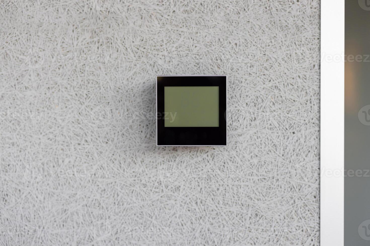 Electronic thermostat mounted on white wall displaying current indoor temperature. Device is sleek, modern, and essential for climate control in a minimalist environment. photo
