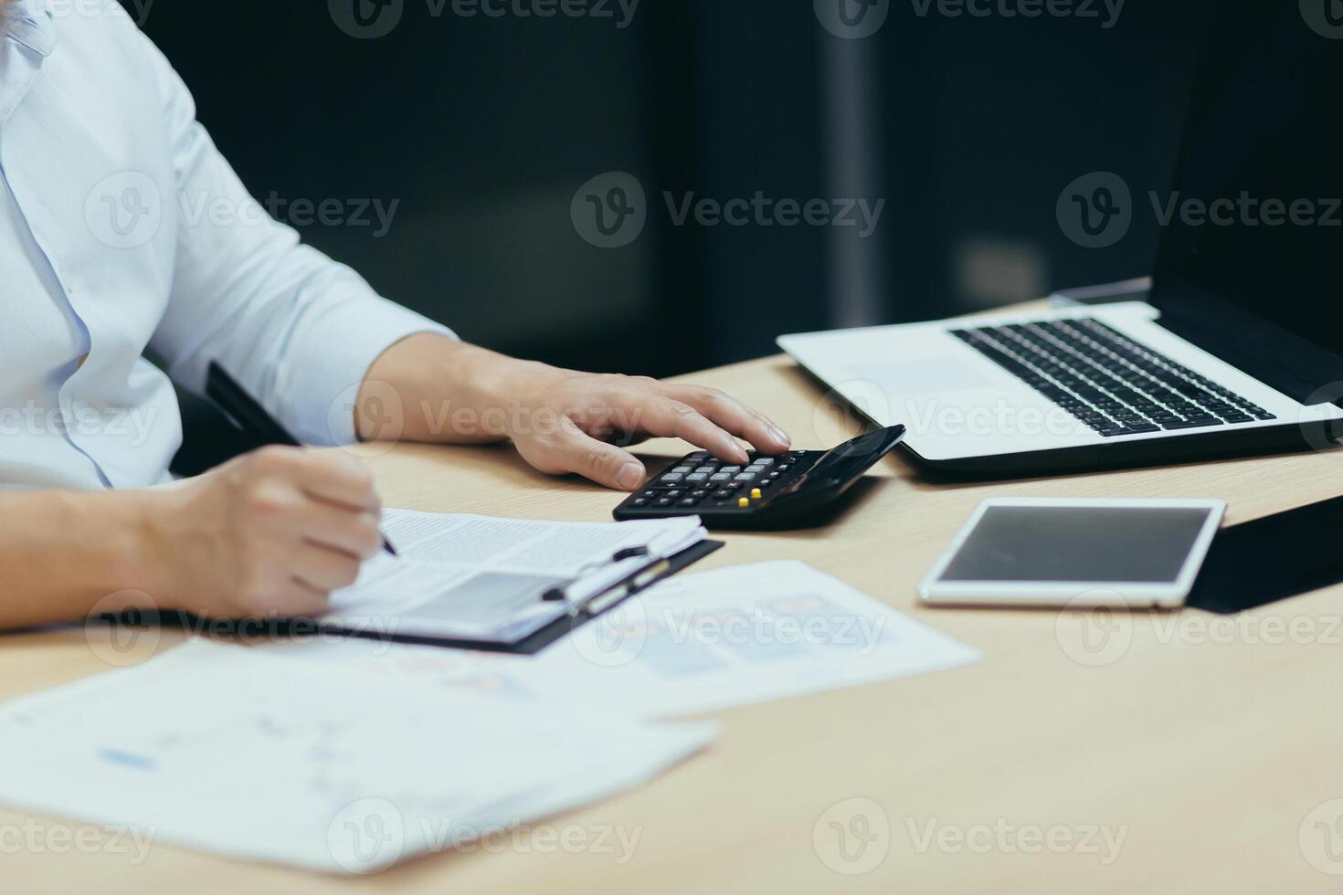 Close-up photo. Male hands in a white shirt at the table in the office with a tablet, laptop, calculator. They write with a pen on paper, sign documents, work with accounts and finances, reports photo