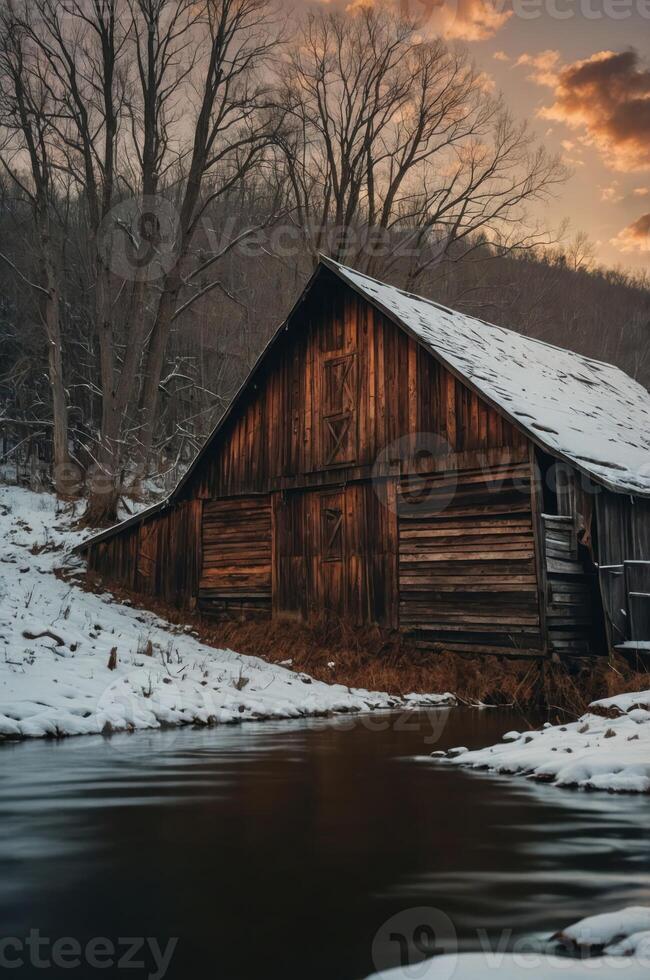 A rustic wooden barn by a snowy river at sunset, evoking tranquility and nature's beauty. photo