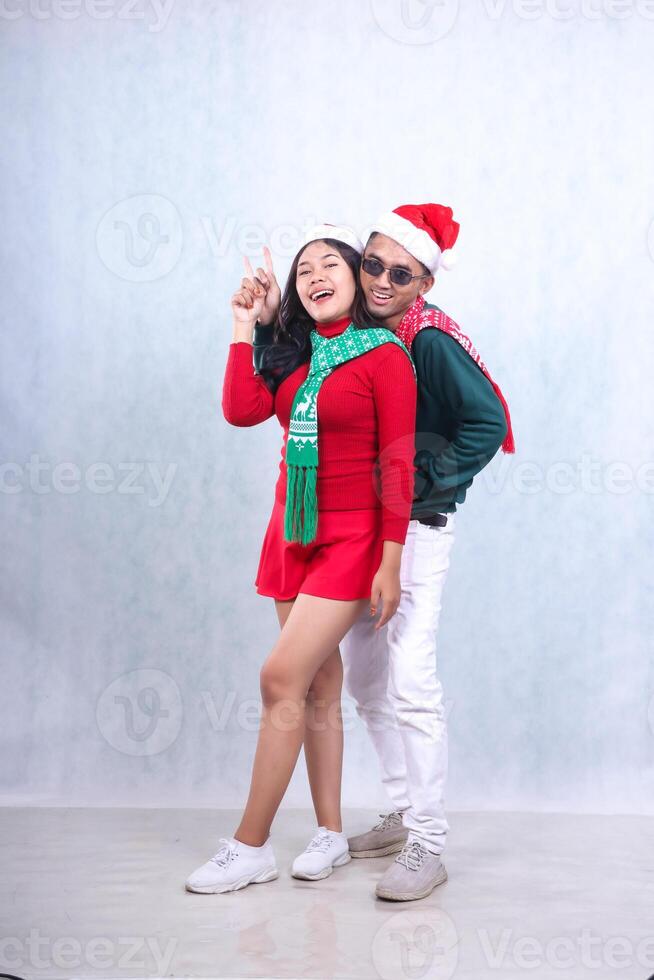 Full body Asian couple wearing party clothes with Santa hats celebrating Christmas and New Year, hands pointing up happily to the camera. isolated on white background photo