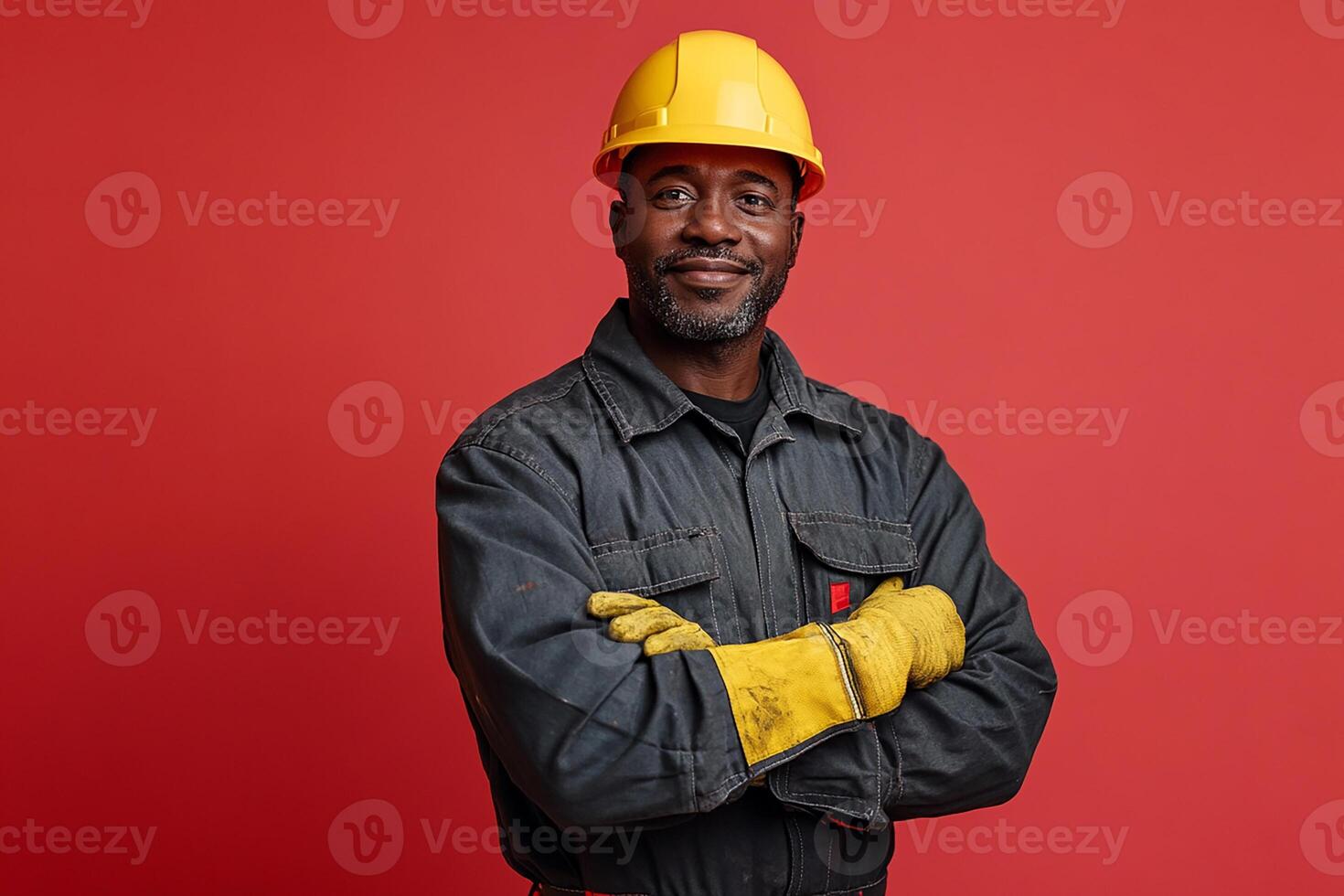 A black man in a hard hat and gloves standing in front of a red background photo