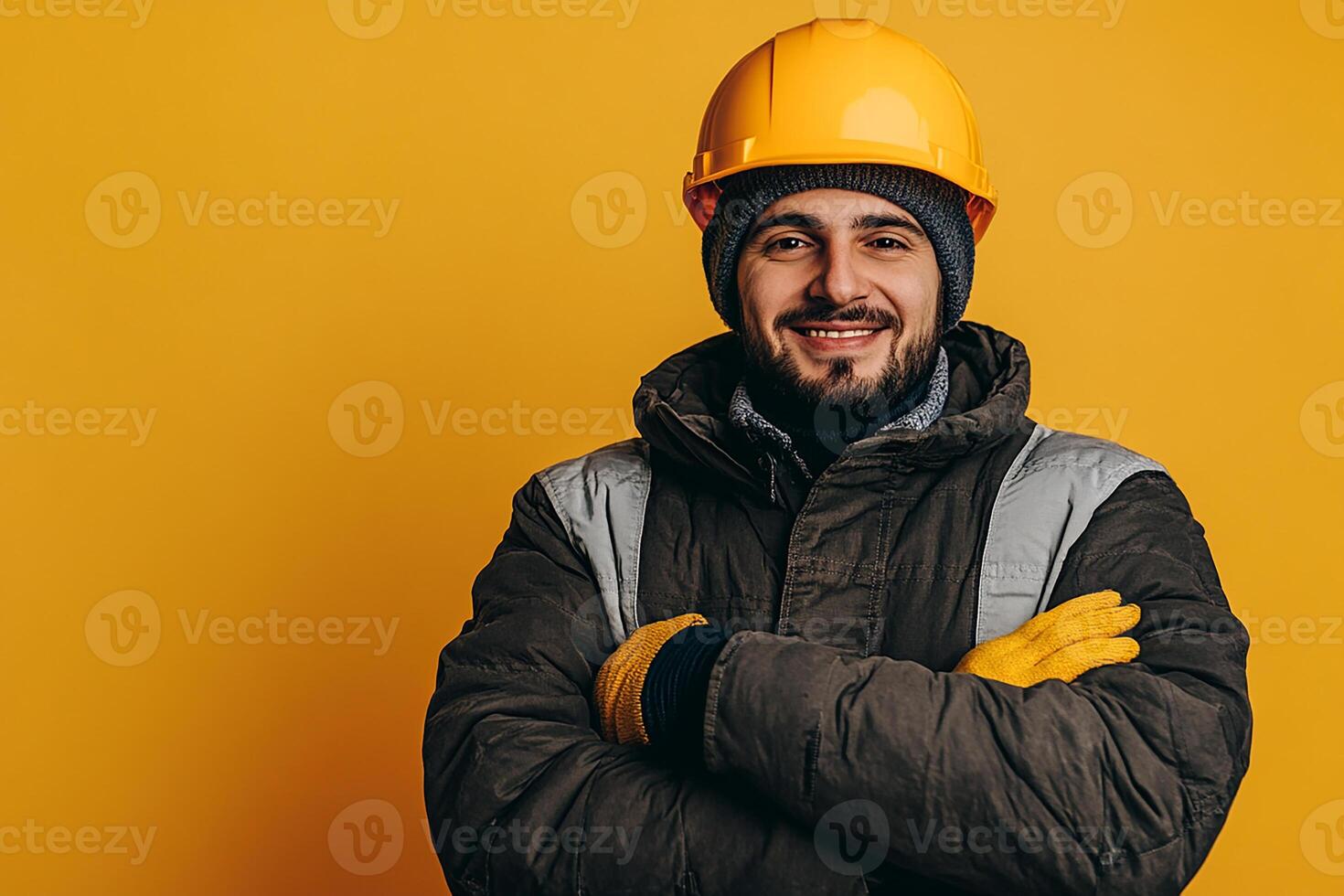 A man in a hard hat and jacket standing in front of a yellow background photo