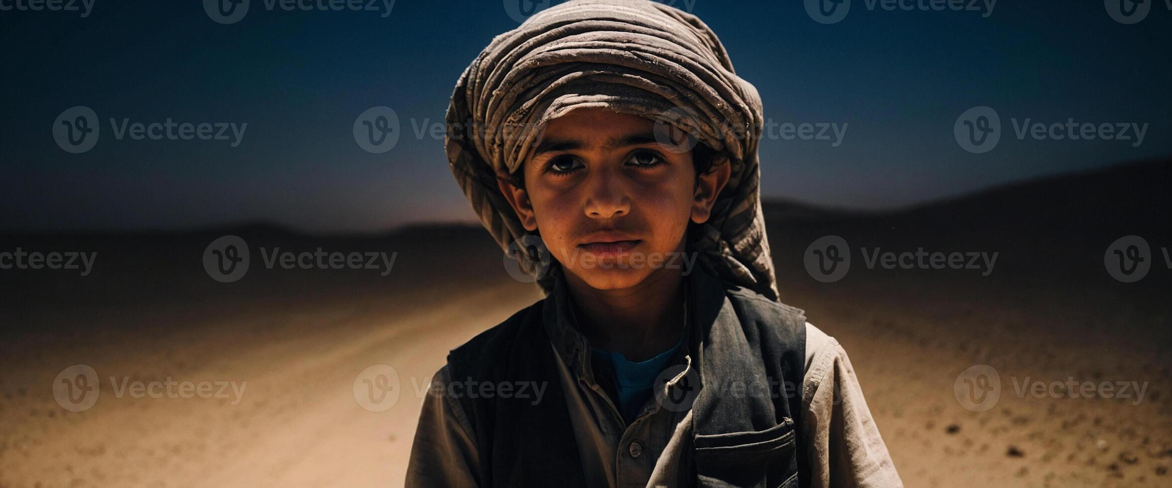 A young boy in a turban standing in the middle of a desert photo
