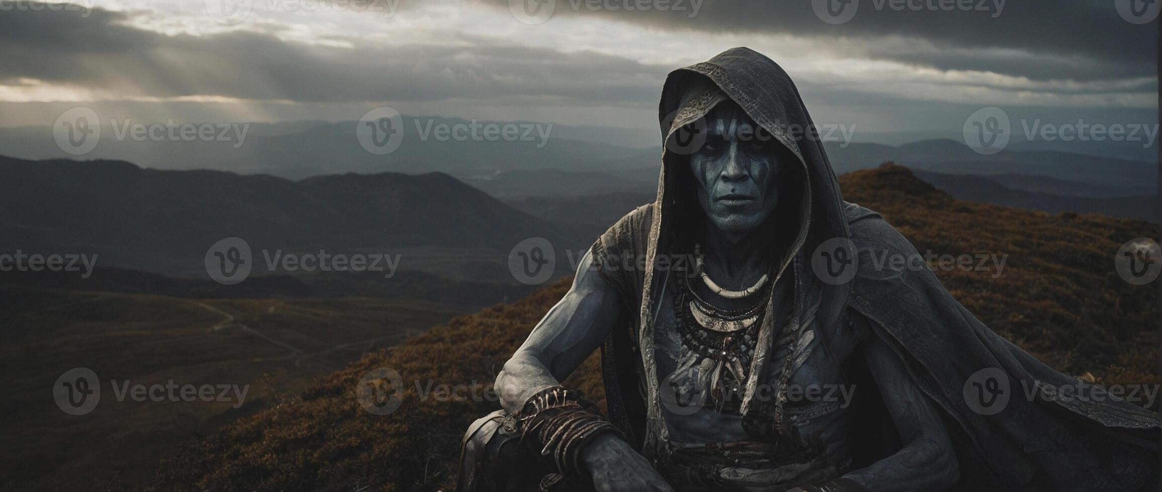 A man in a hooded robe sitting on top of a mountain photo