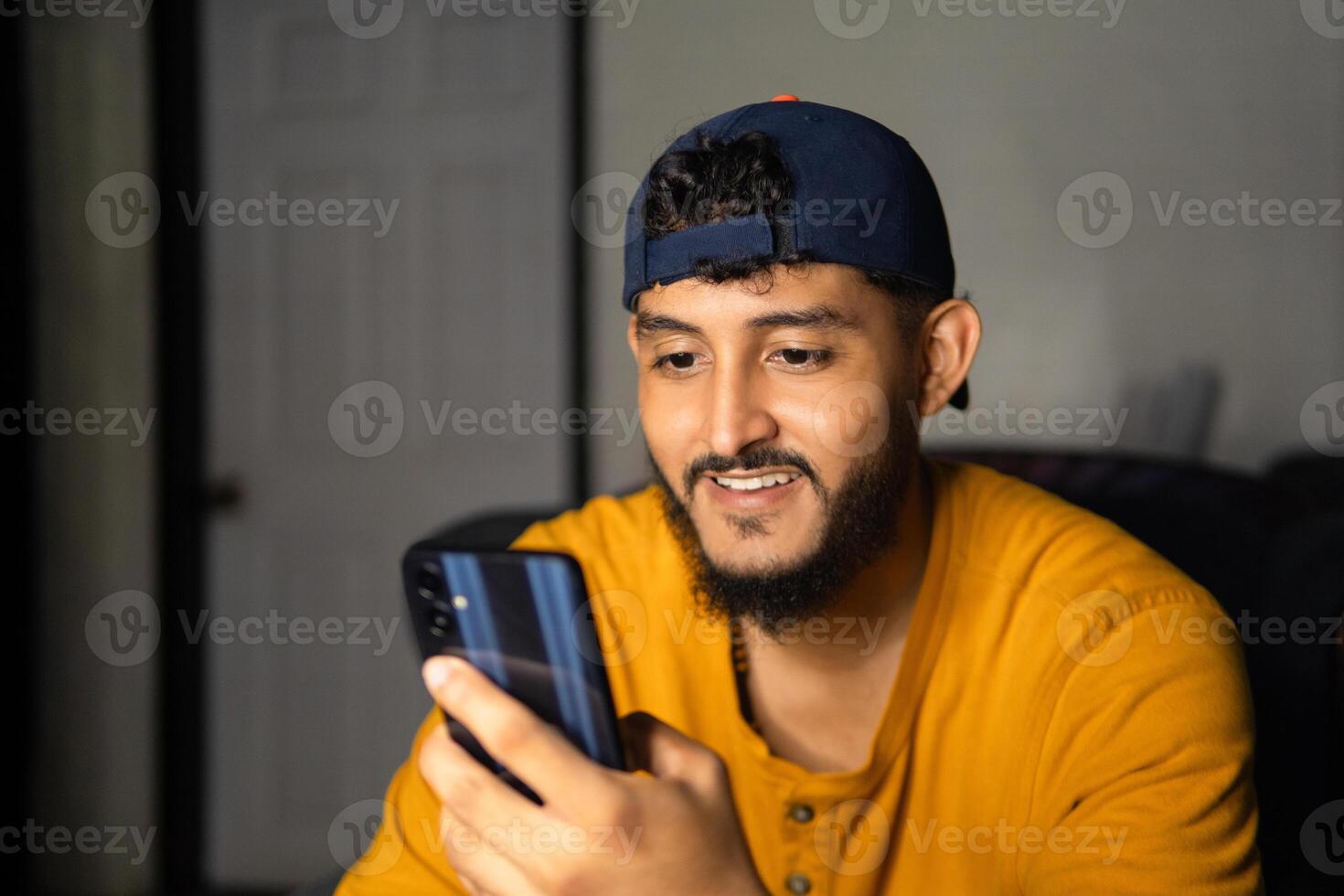 Young man wearing a baseball cap is using a smartphone at home photo