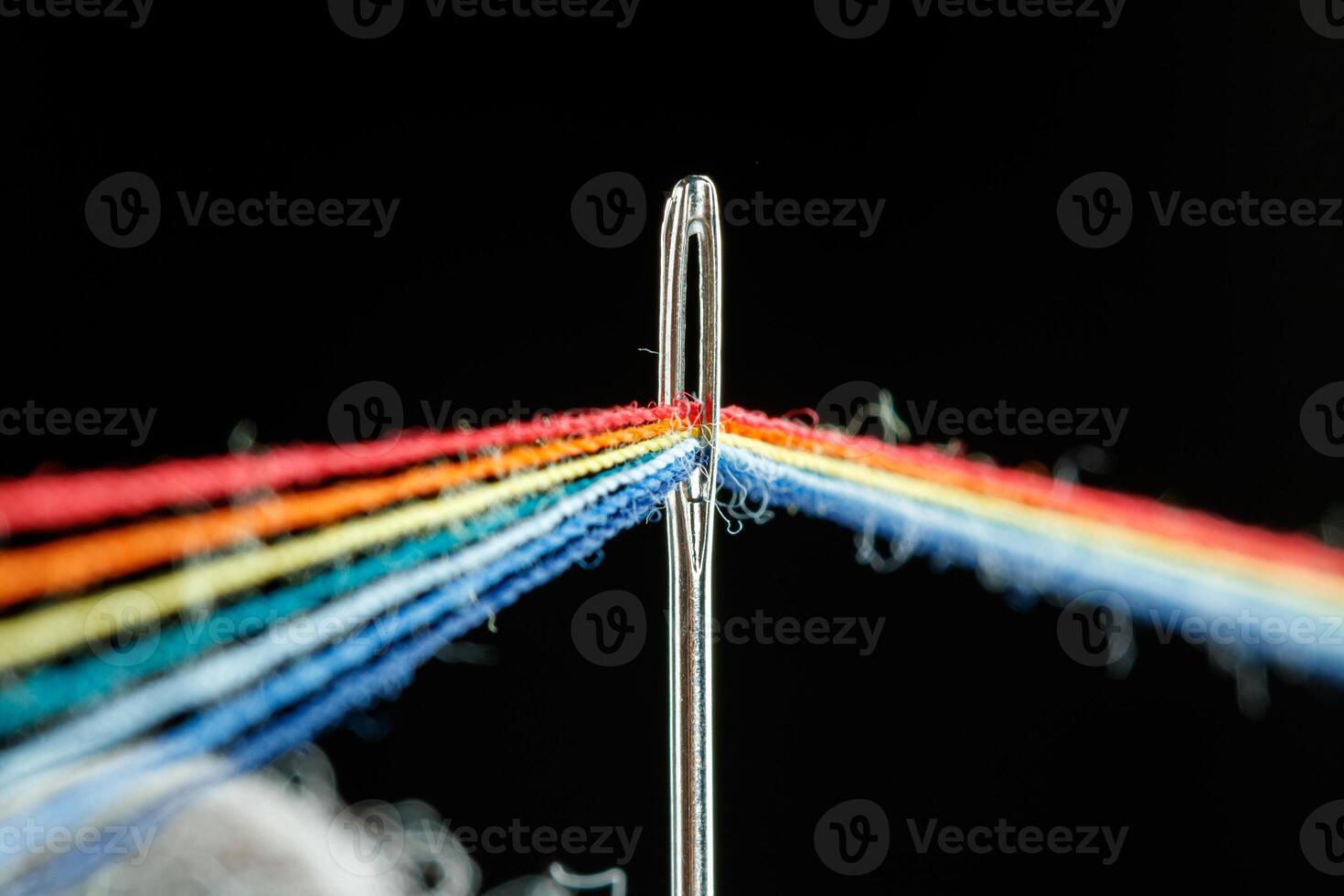 multi-colored threads for sewing in the form of a rainbow pass through an antique needle on a black background photo