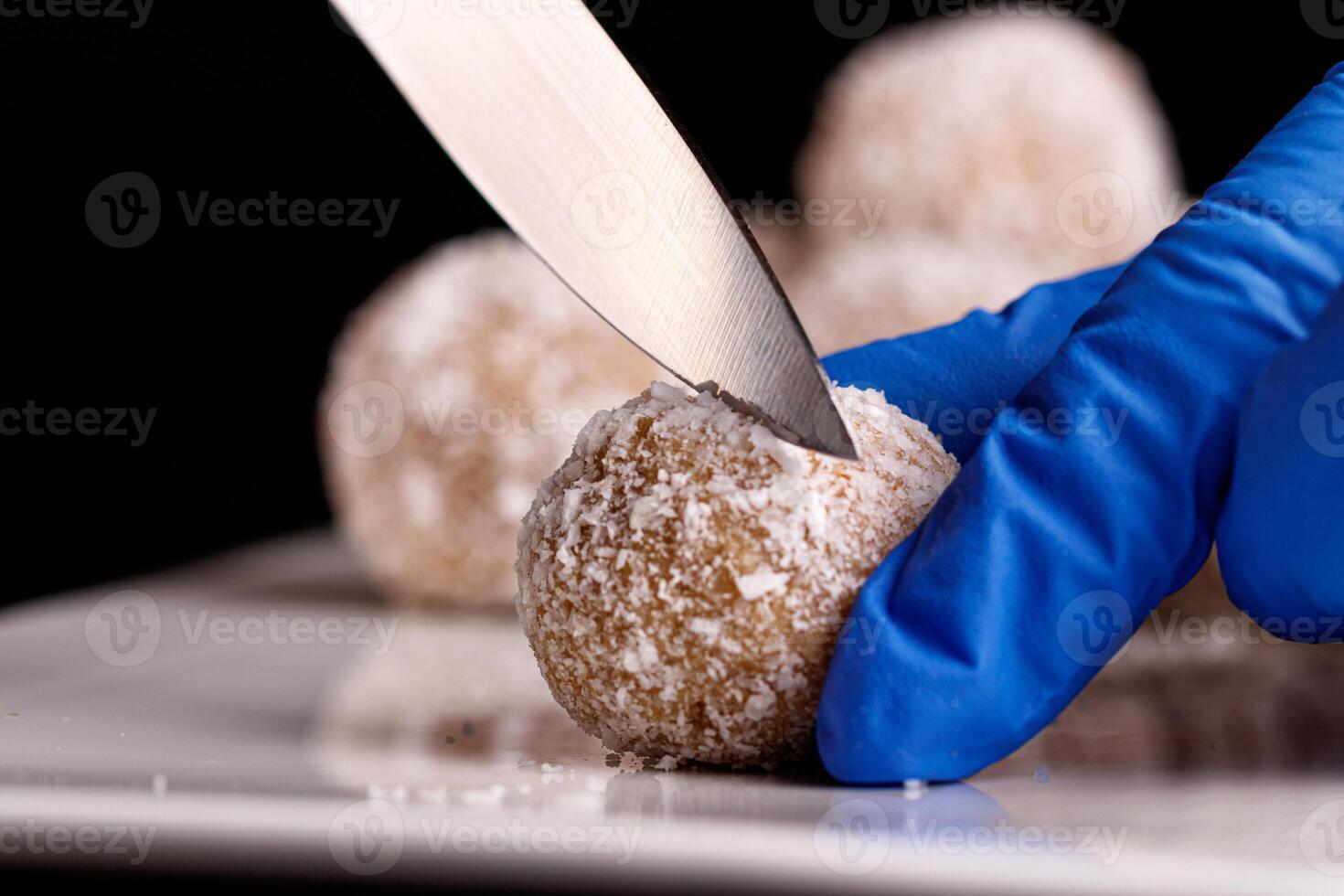 Beautiful sweets with coconut are cut with a knife on a white plate on a black background photo