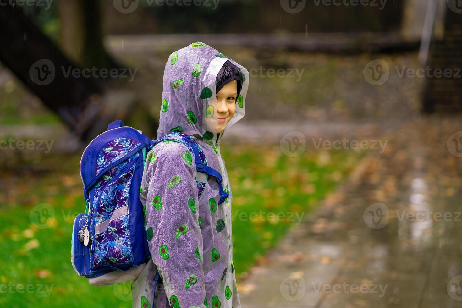 A child in a raincoat with a school bag goes to school in the rain photo