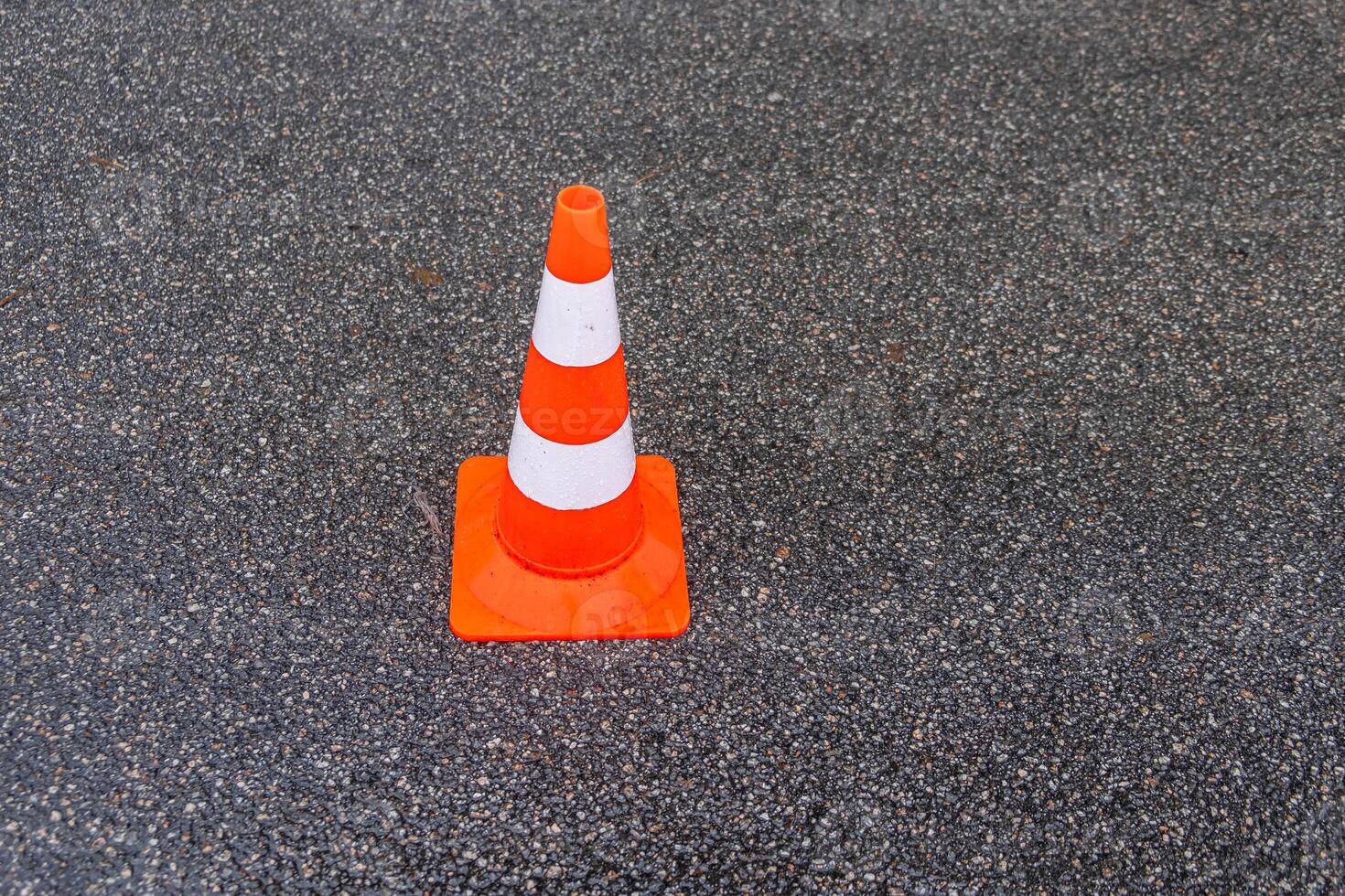 traffic cone, white and orange stripes on gray asphalt, copy space. Construction cones marking part of road with a layer of fresh asphalt. photo