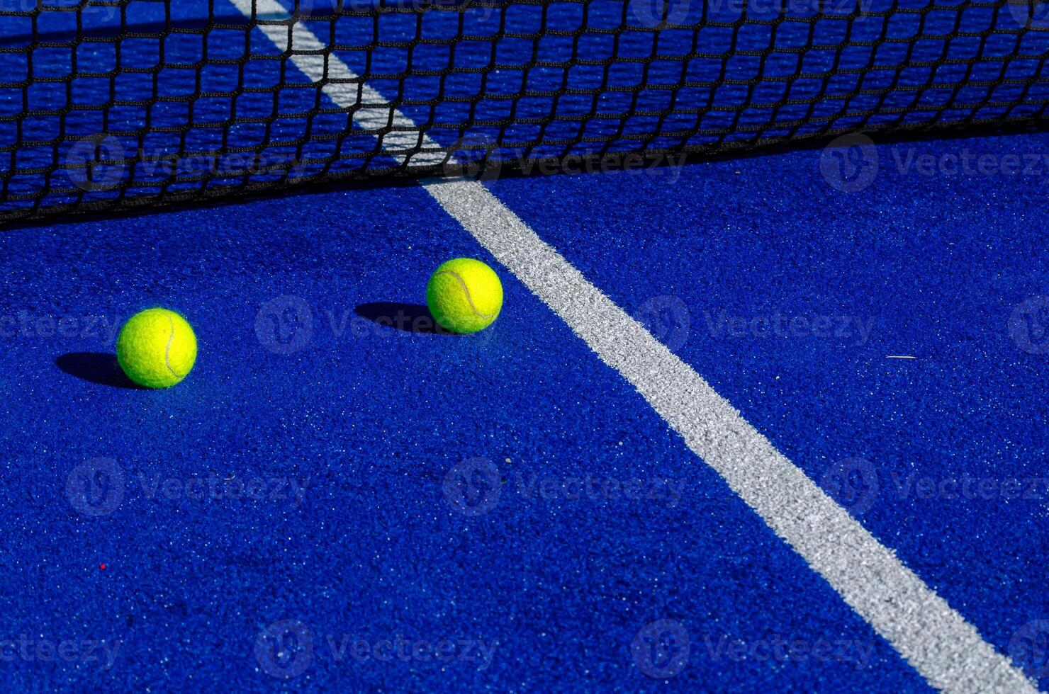 Two balls next to the net of a paddle tennis court. photo