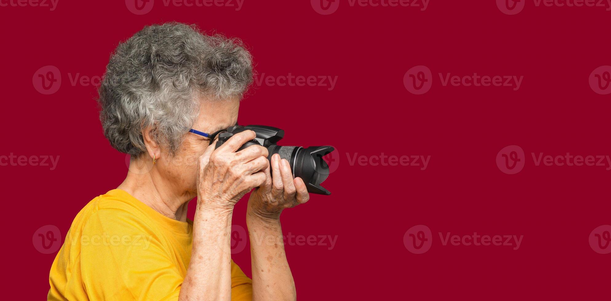 Senior woman taking photographs with a digital camera while standing on a red background photo
