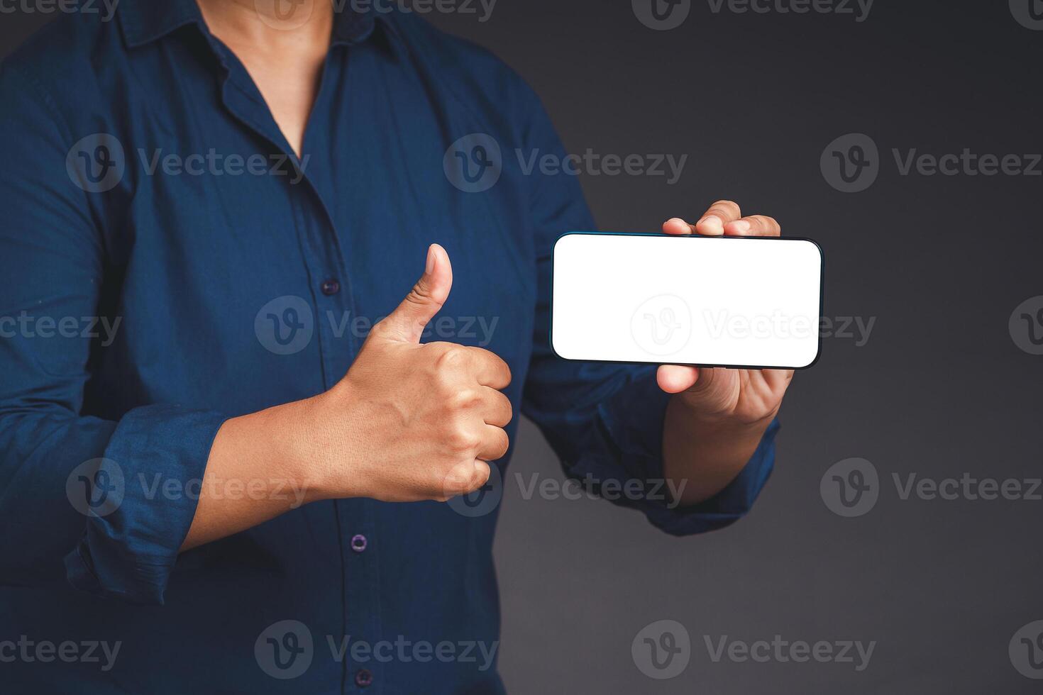 Hand holding a horizontal mobile phone with a blank white screen and showing thumbs up while standing on a gray background photo