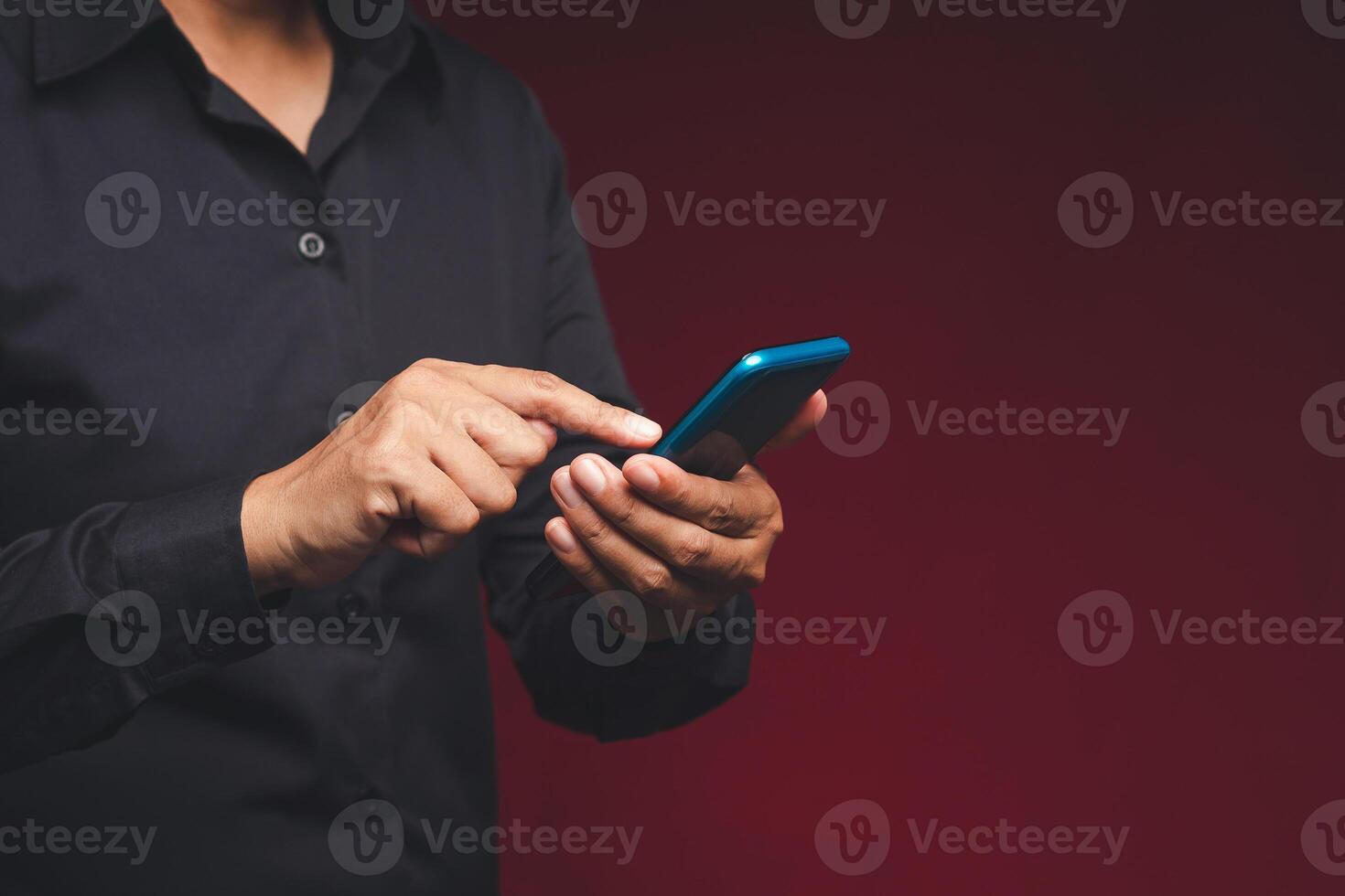Close-up of hands businessman in a black shirt using a mobile phone while standing on a red background photo