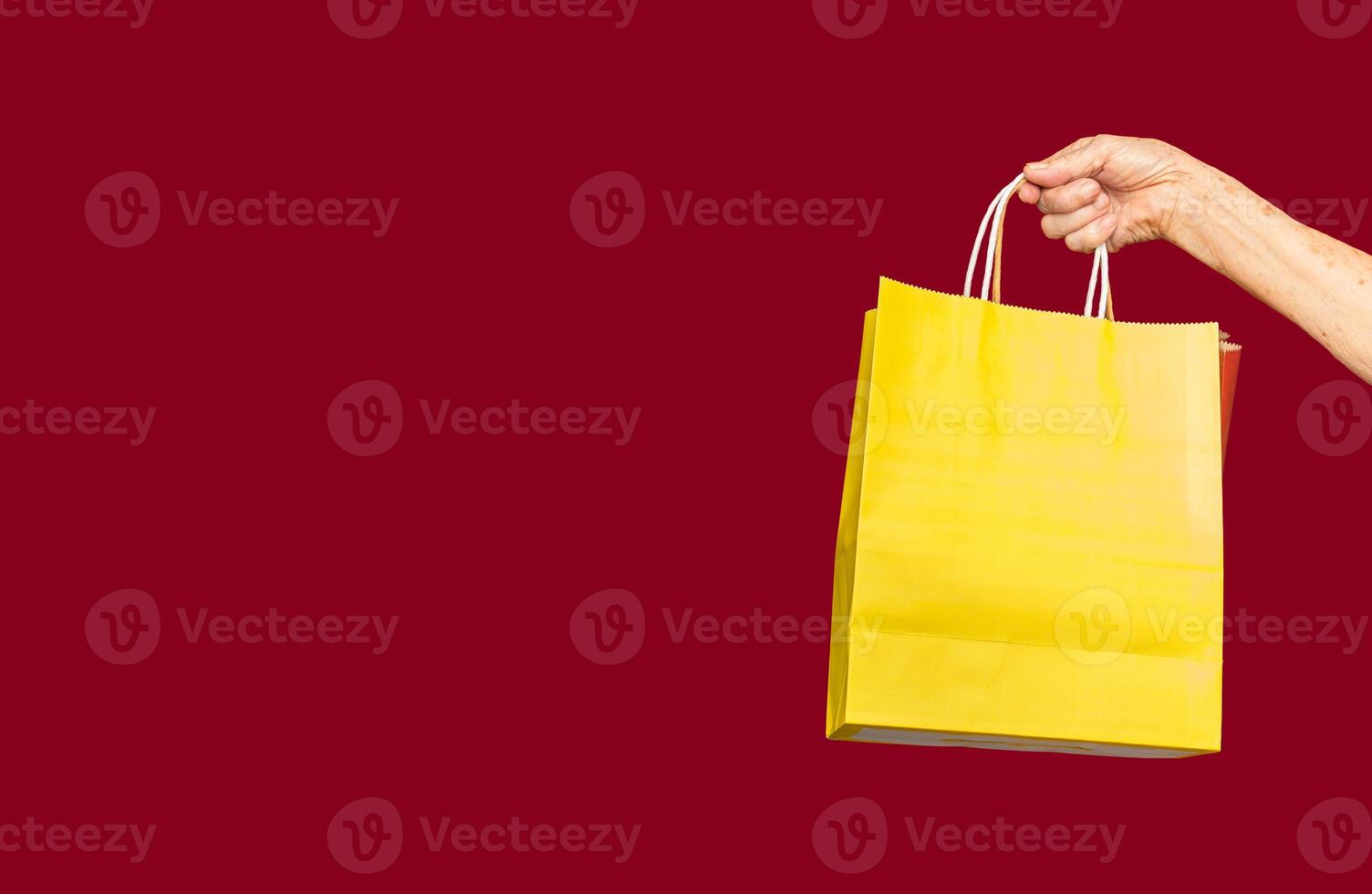 Hand holding yellow and red shopping bags against a red background photo