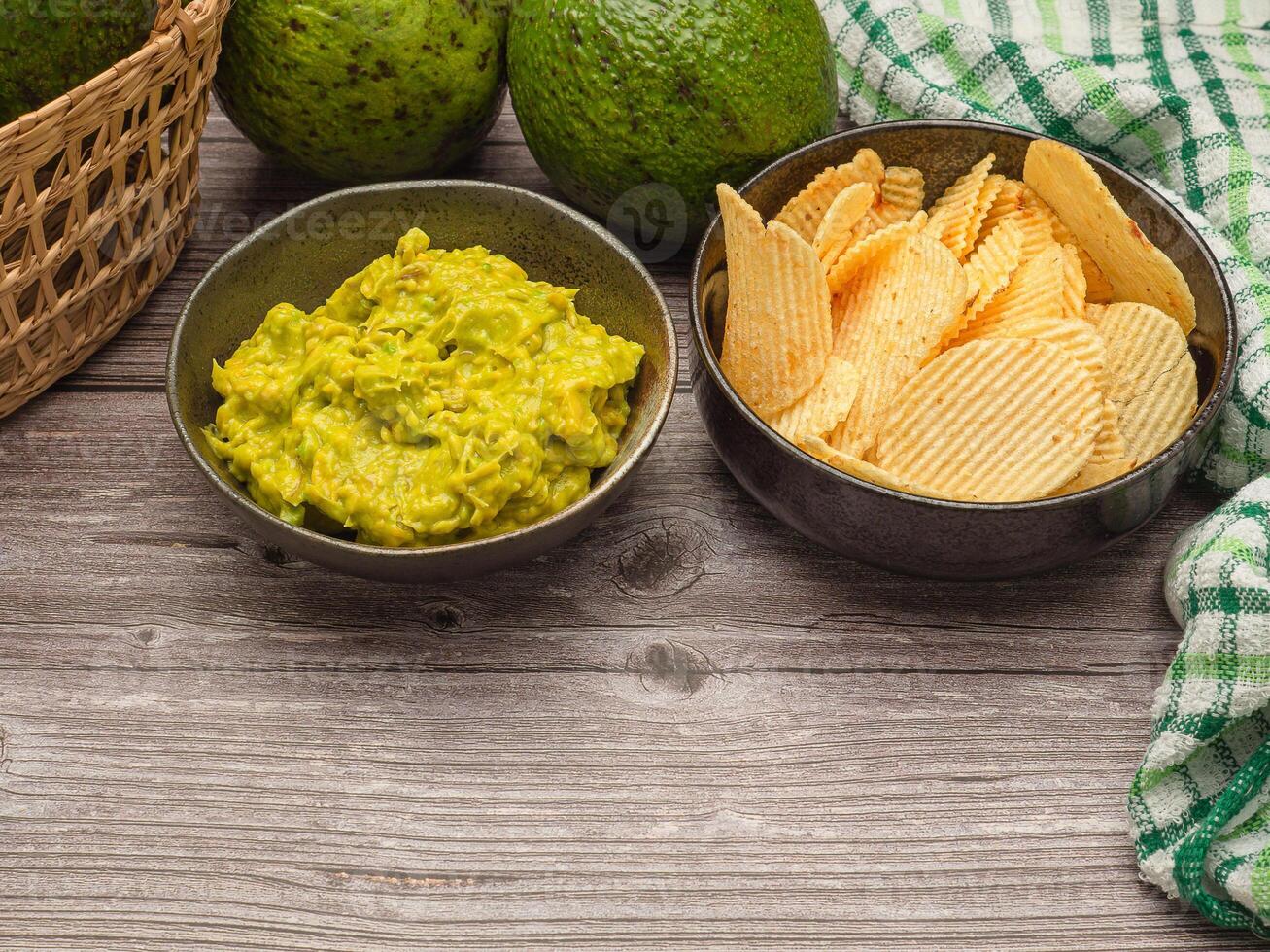 Top view of fresh guacamole in a dish and potato chips on a plate over a wooden table photo