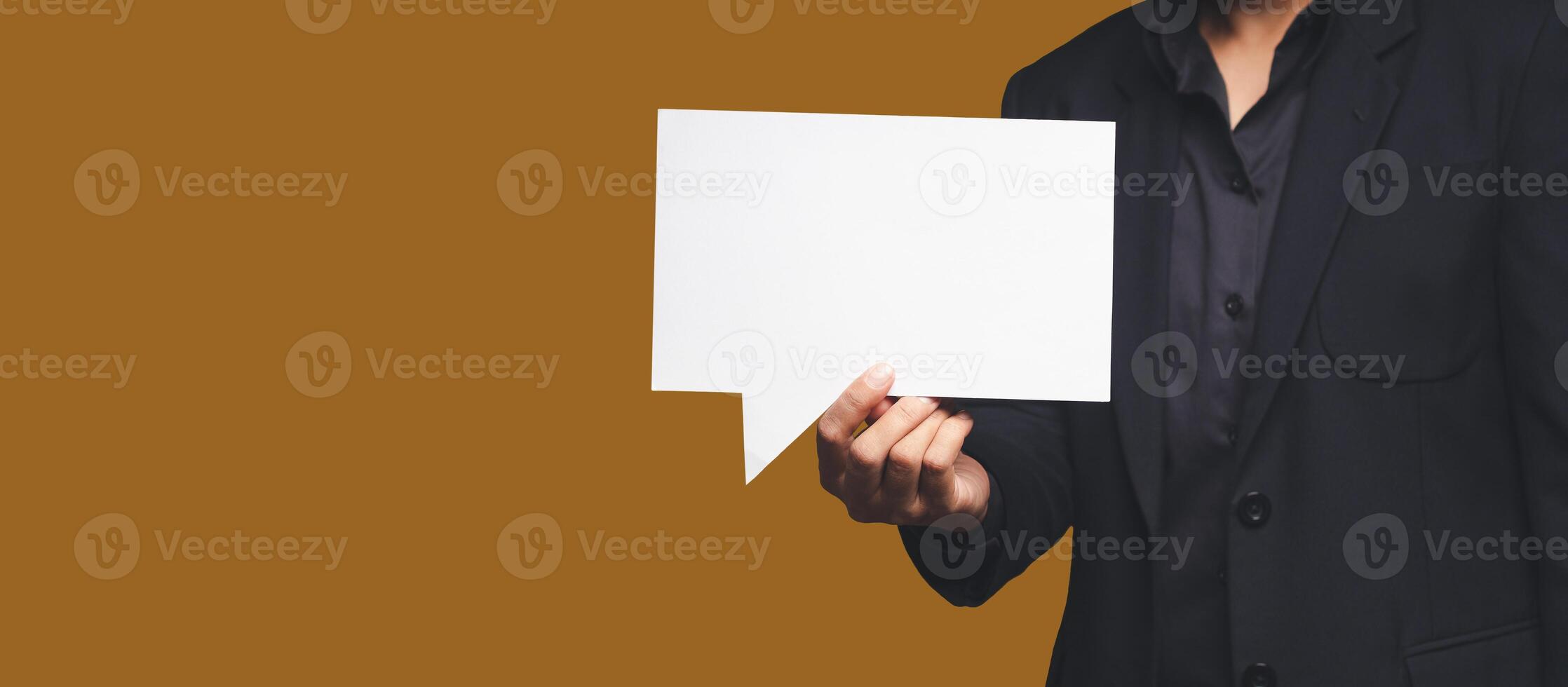 Businessman in a suit holding a blank white speech bubble while standing on an orange background photo
