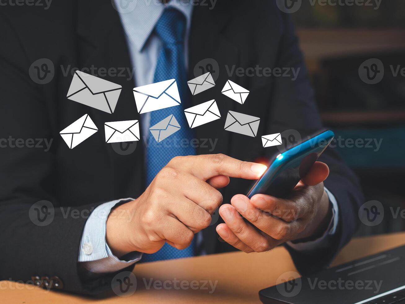 Businessman holding a smartphone receives a new message with email icons while sitting in the office photo