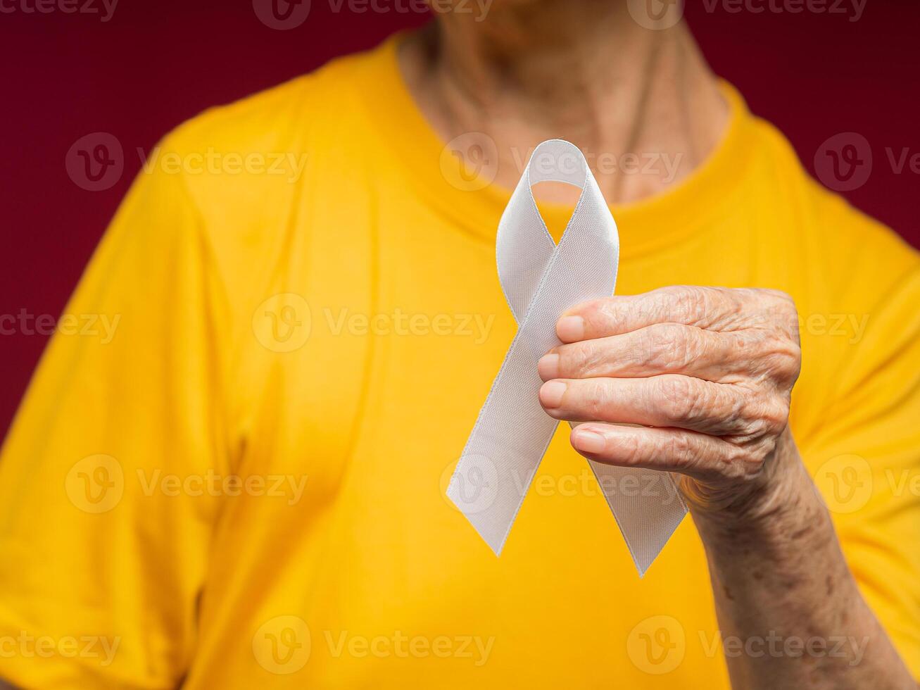 A senior woman's hand is holding a white ribbon while standing on a red background photo