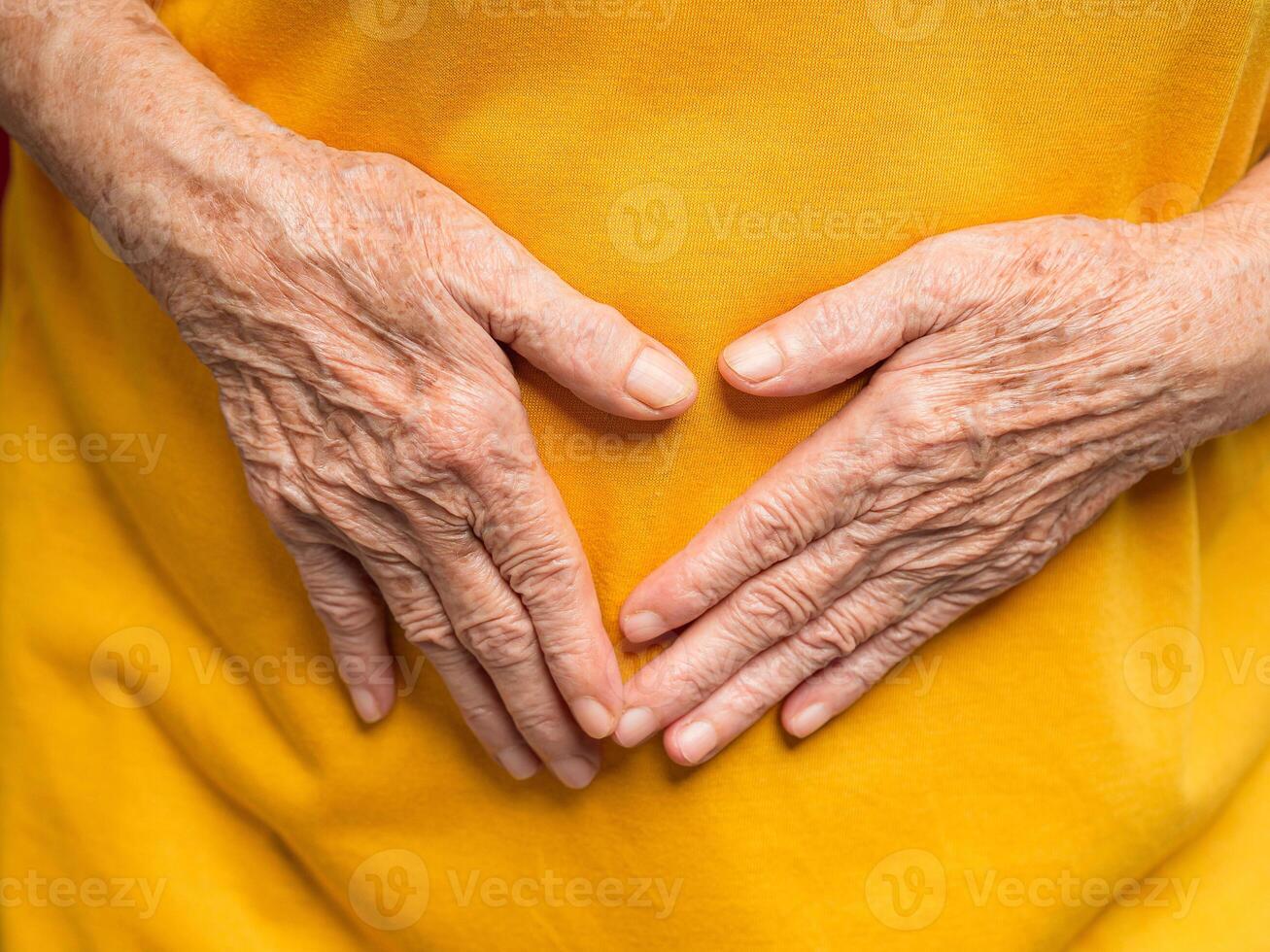 A close-up of an older woman's hands touches her belly suffering from abdominal pain while standing on a red background photo