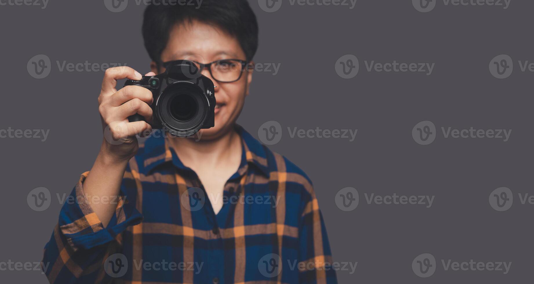 Portrait of a photographer in a blue shirt holding a digital camera while standing on a gray background photo