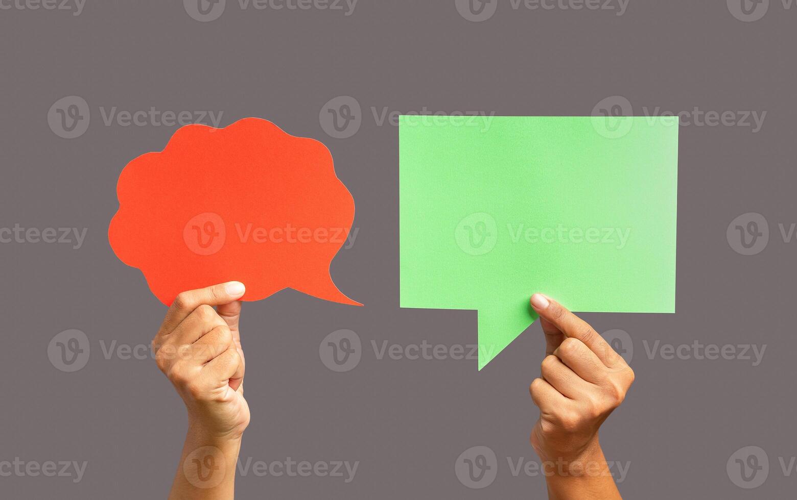 Close-up of hands holding a red and a green speech bubble against a gray background photo