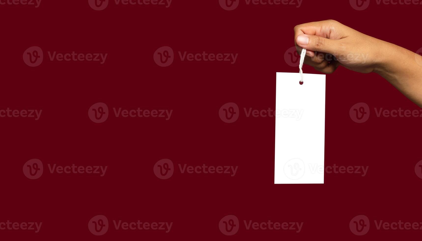 Hand holding a blank white label or price tag against a red background photo
