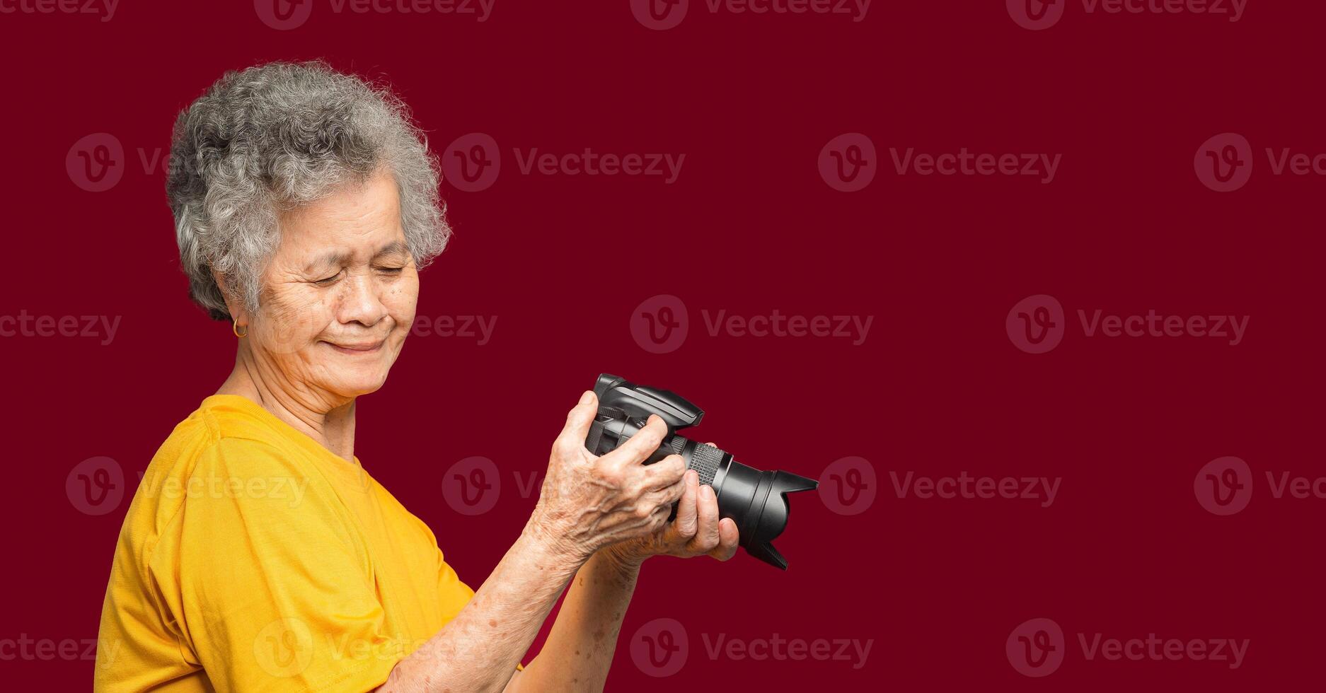 Happy senior woman looking at her photos in a digital camera while standing on a red background