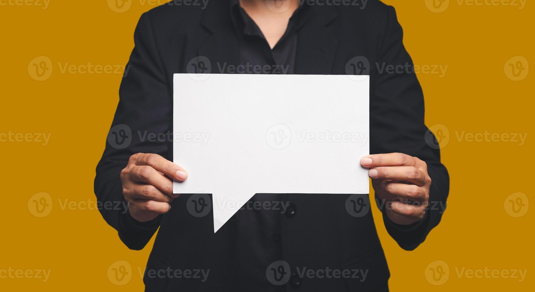 Businessman in a suit holding a blank white speech bubble while standing on an orange background photo