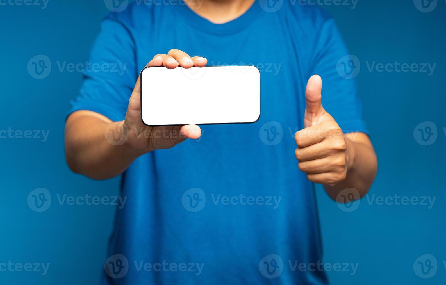 Hand holding a horizontal mobile phone with a blank white screen and showing thumbs up while standing on a blue background photo