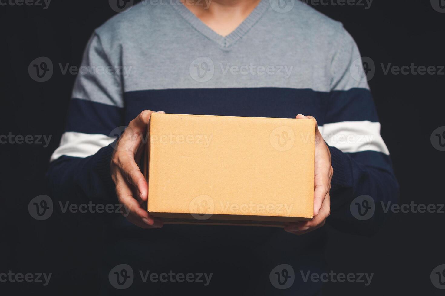 Man in a sweater holding a cardboard box while standing on a black background photo