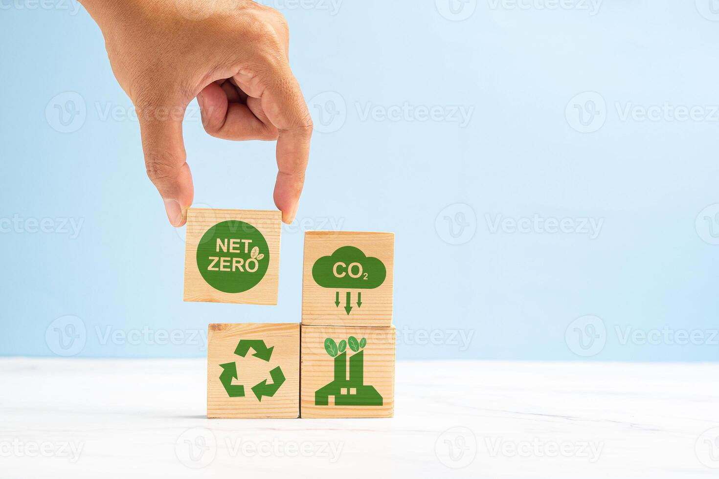 Net-zero CO2 emissions target in 2050. Hand holding of a wooden cube with green icons over a marble floor against a light green background photo