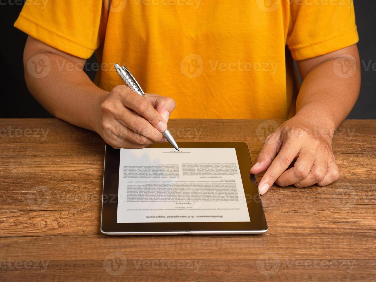 Hand of a man in an orange casual signing on lease contract or agreement on a tablet while sitting at the table photo