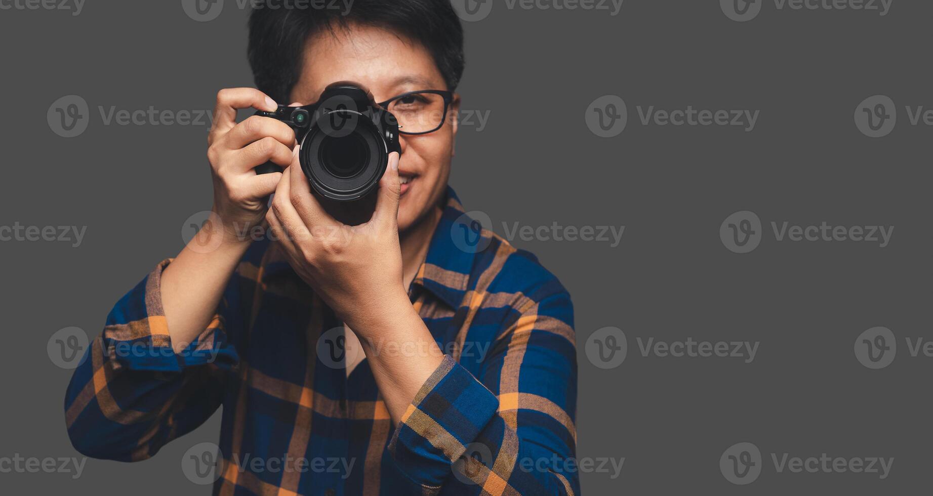 A Photographer holding a digital camera while standing on a gray background photo
