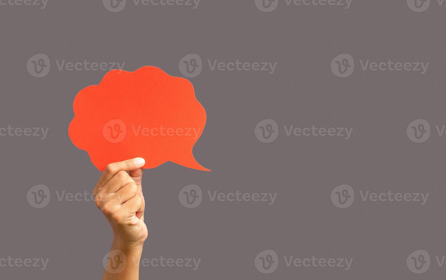 Close-up of hand holding a red speech bubble against a gray background photo
