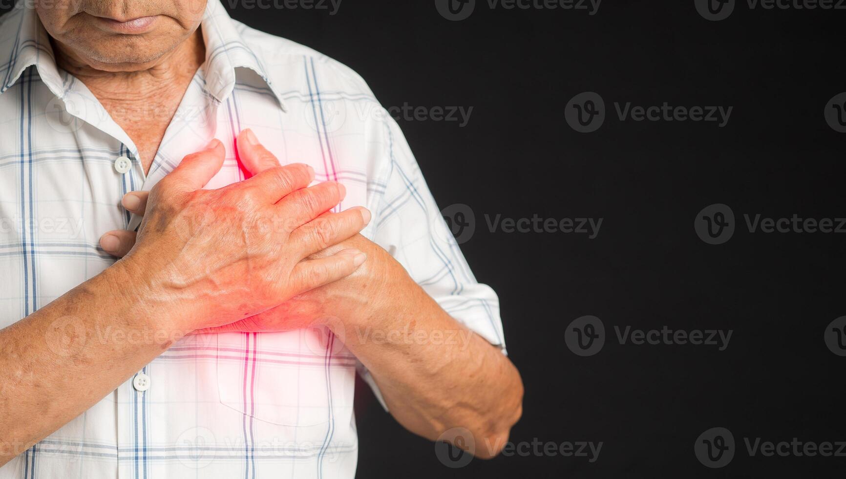 A senior man in a white shirt has sore left chest pain while standing on a black background photo