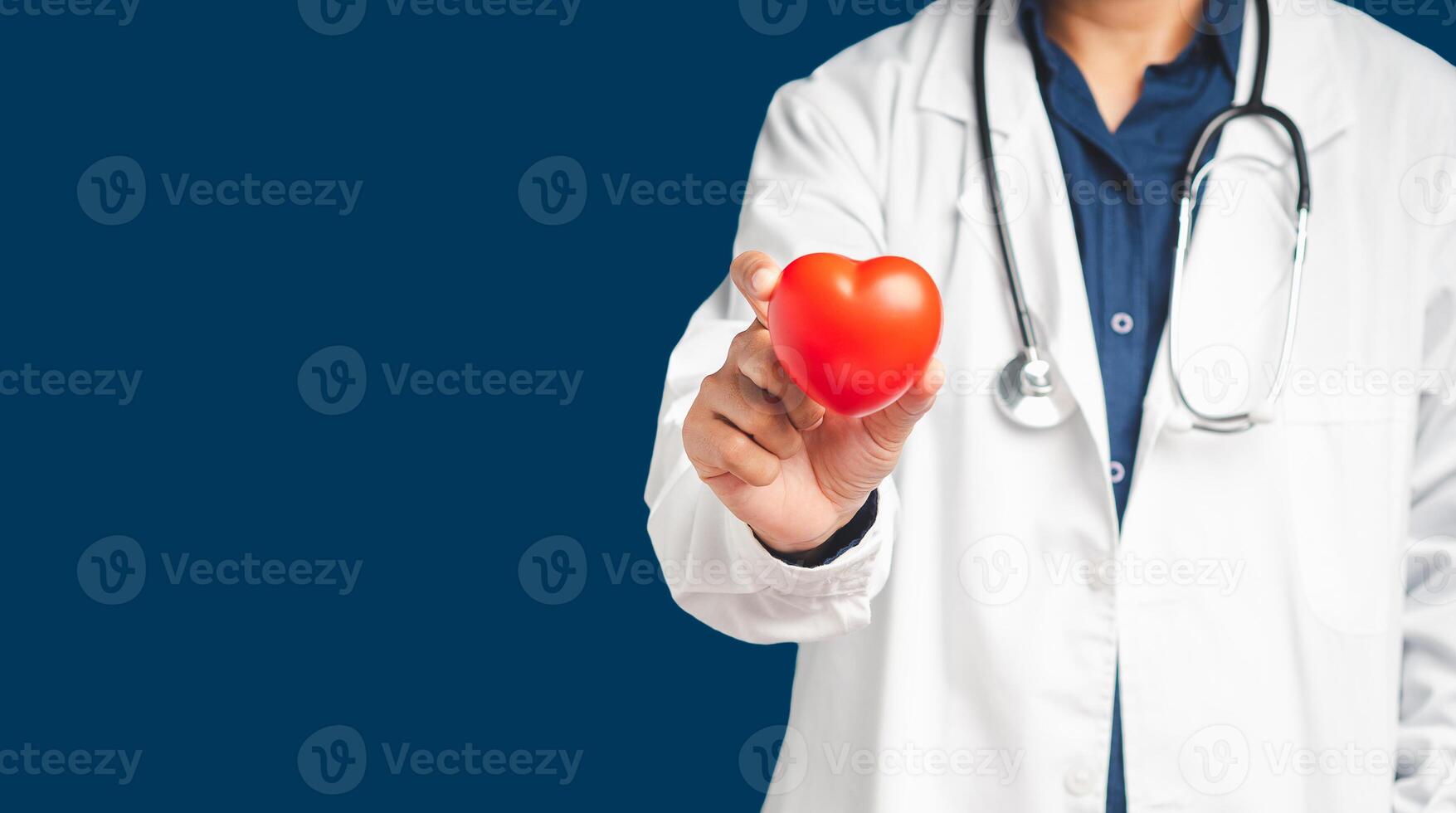Doctor in uniform holding holding a red heart shape while standing on a blue background photo